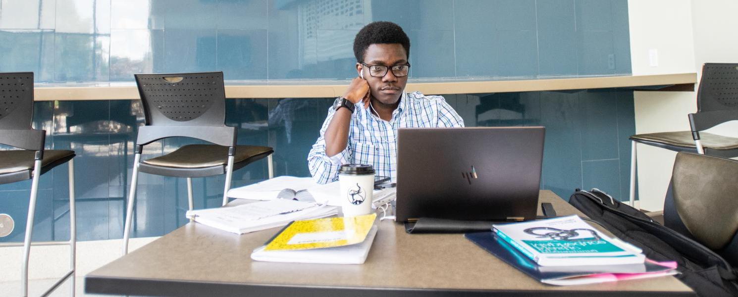 Graduate student studying with a laptop and books.